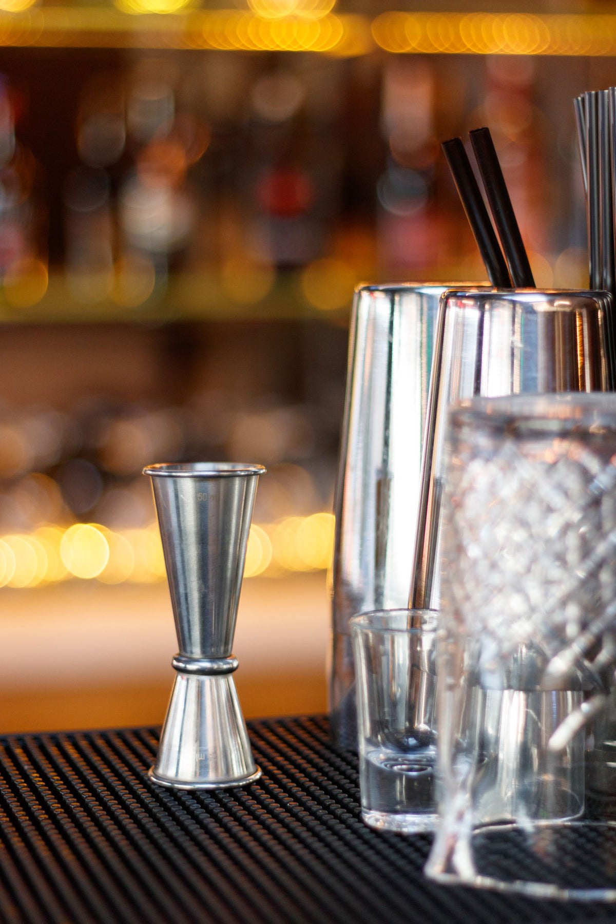 A jigger, cocktail shaker and glassware set out on a bar counter