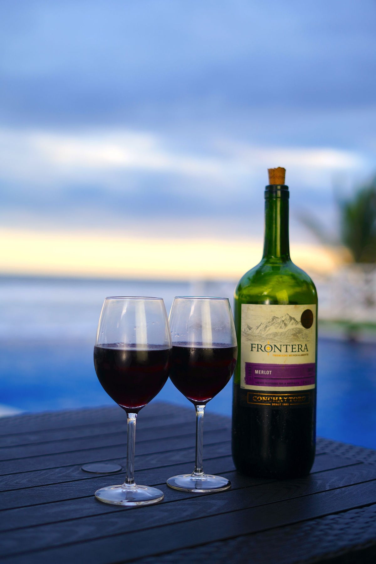Two glasses of red wine poured on a wooden table at sunset