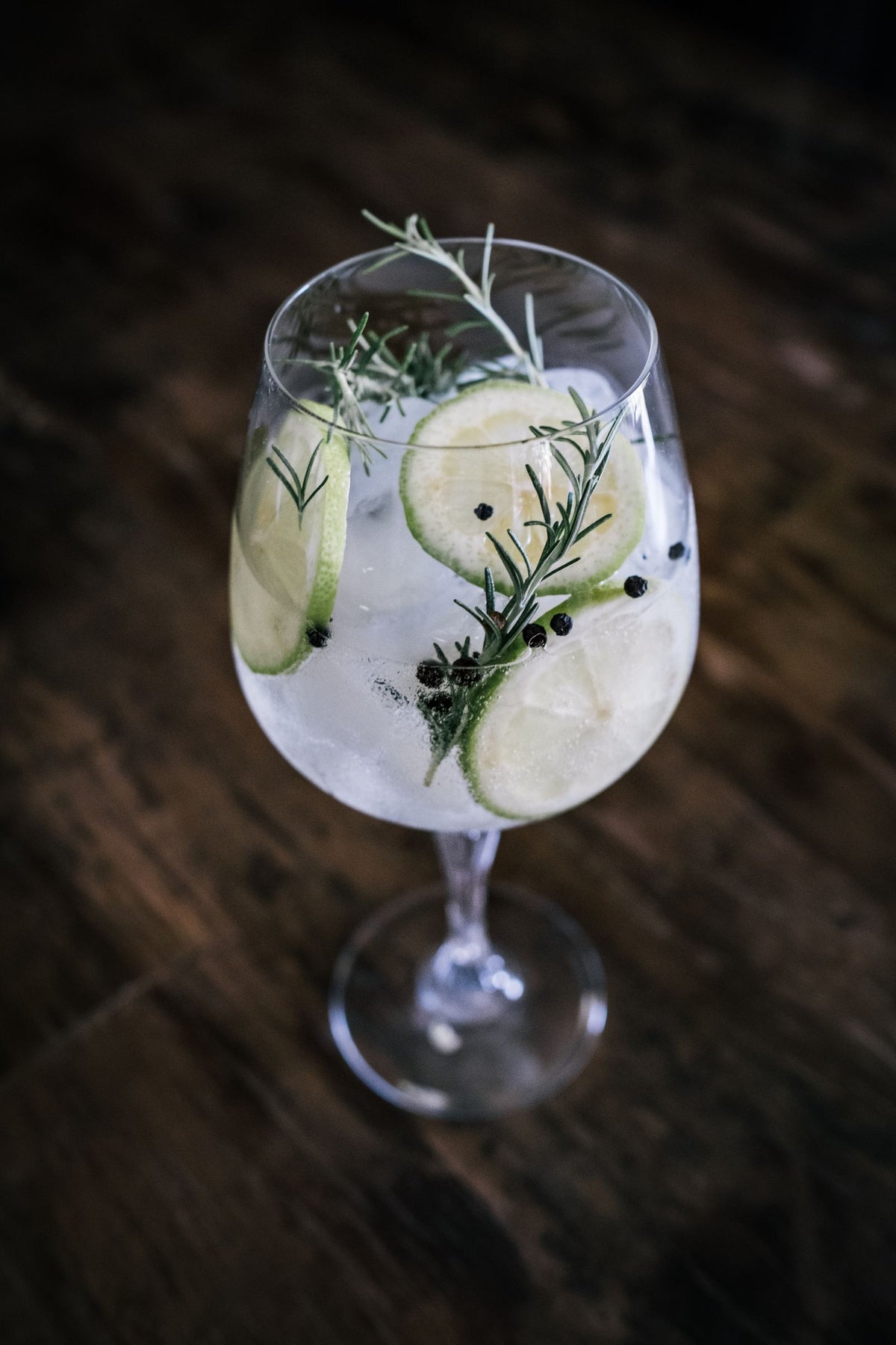 Gin and tonic in a glass garnished with lime, rosemary and juniper berries