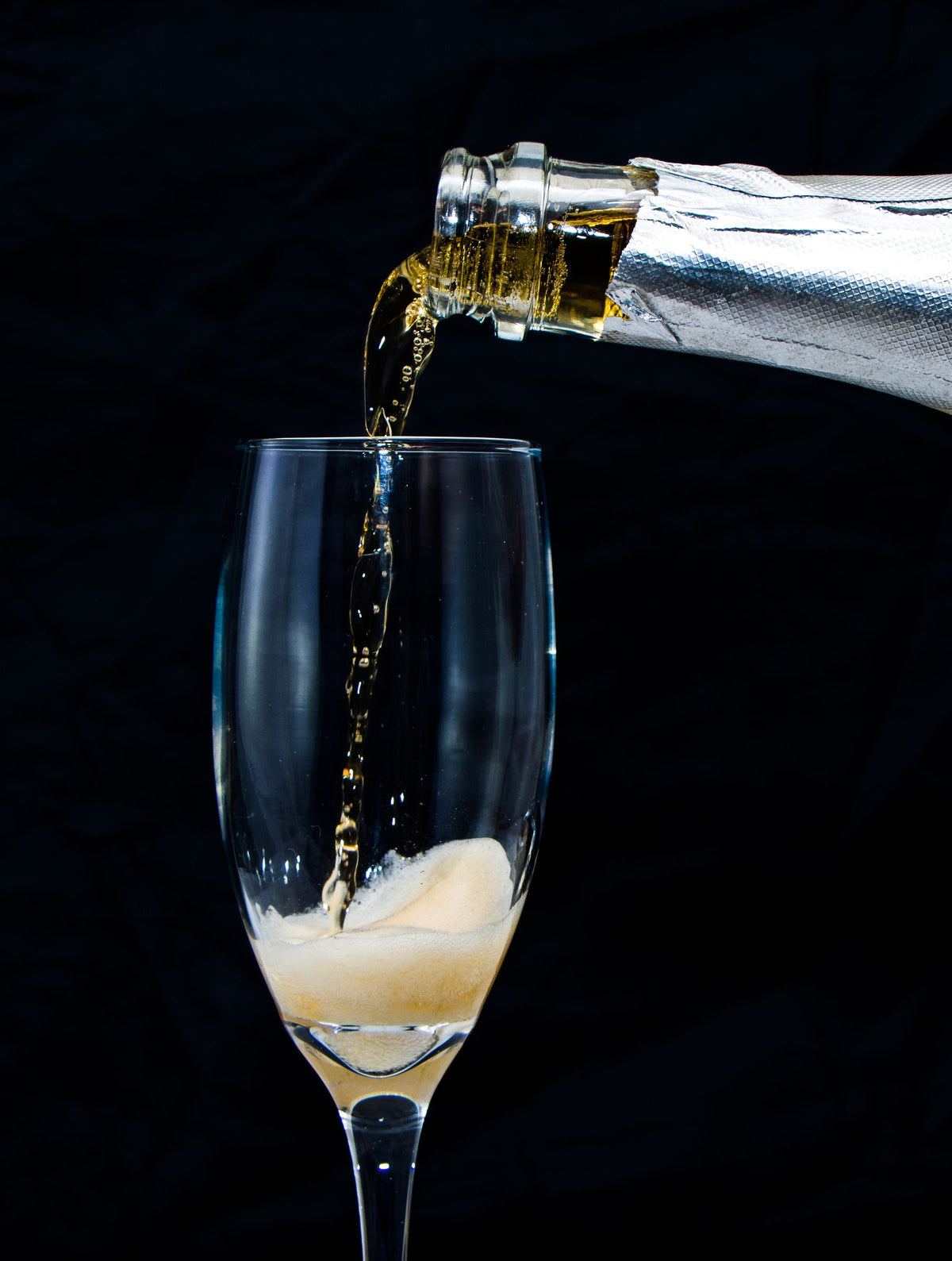 Sparkling wine being poured into a flute against a black background