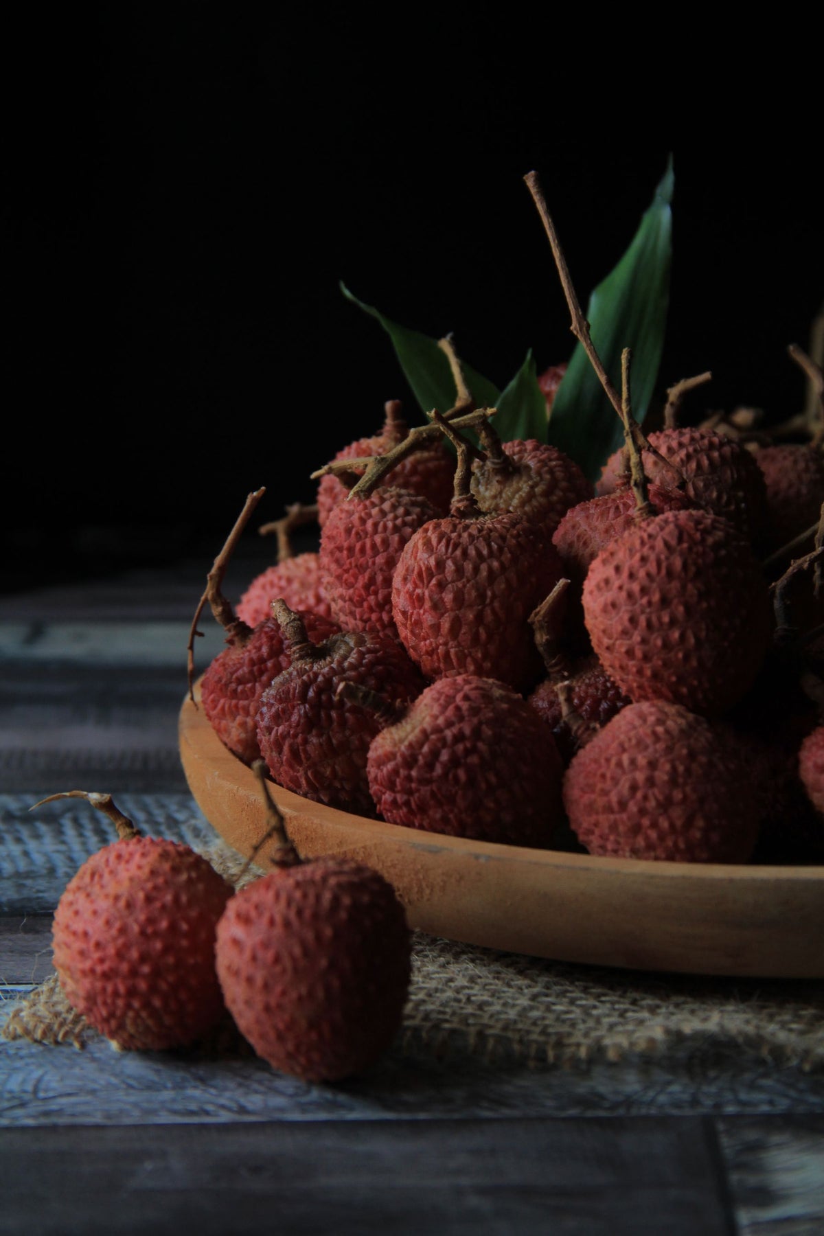 Fresh red lychees on a wooden board against a dark background