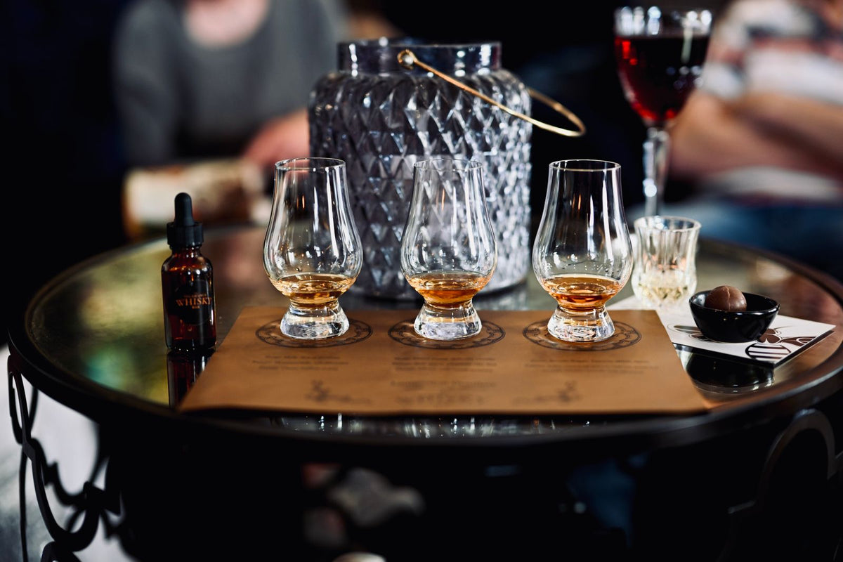 A flight of whisky glasses set out on a wooden tasting board