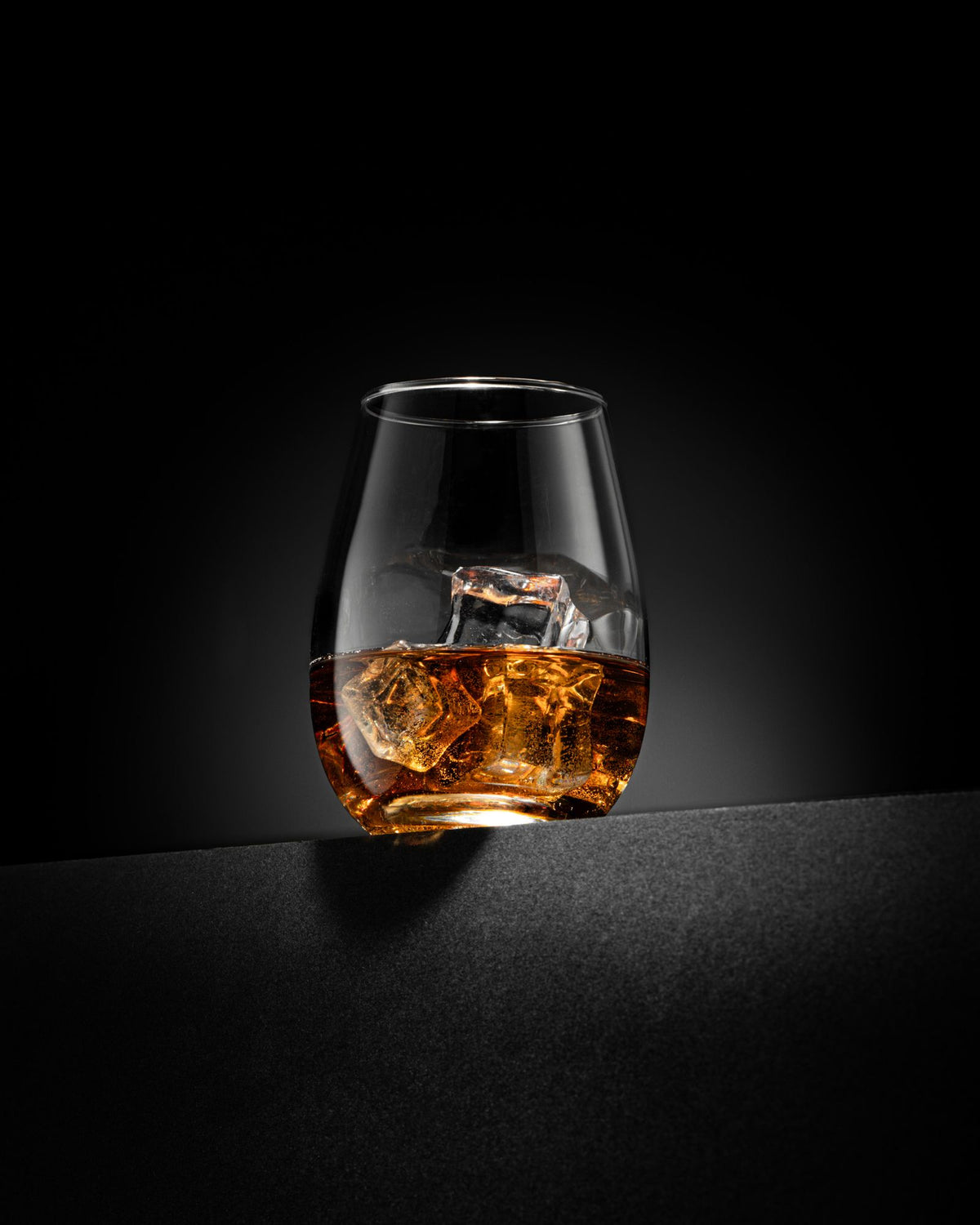 A glass of whisky with ice cubes against a dark background