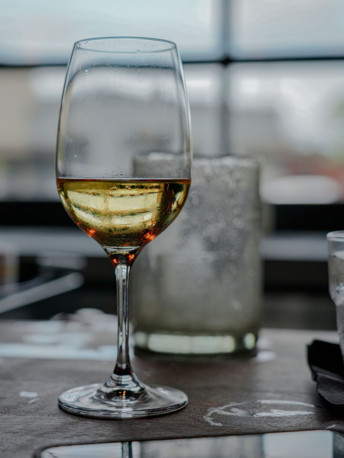 A chilled glass of white wine on a table by a window