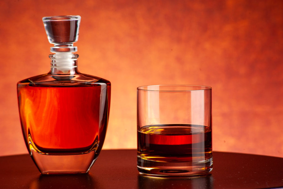 A whiskey decanter and a filled glass on a warm dark background