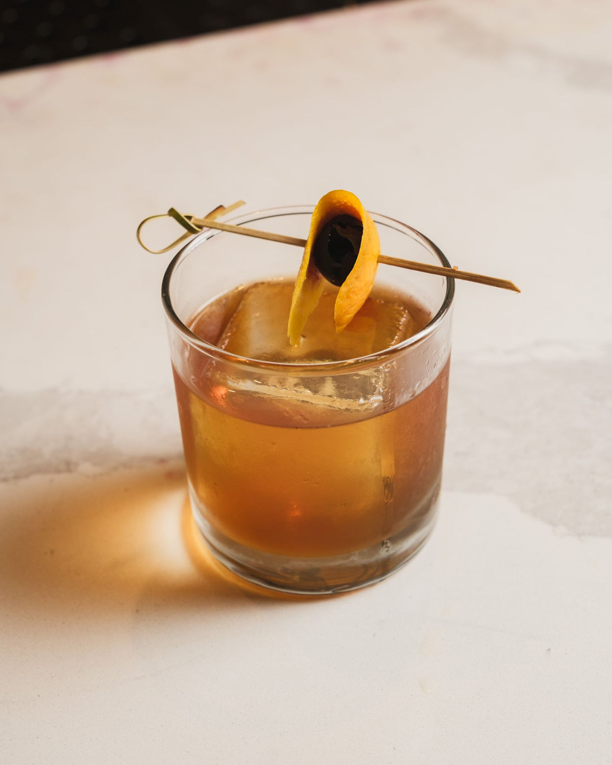 Old fashioned cocktail with ice and orange twist on a marble bar