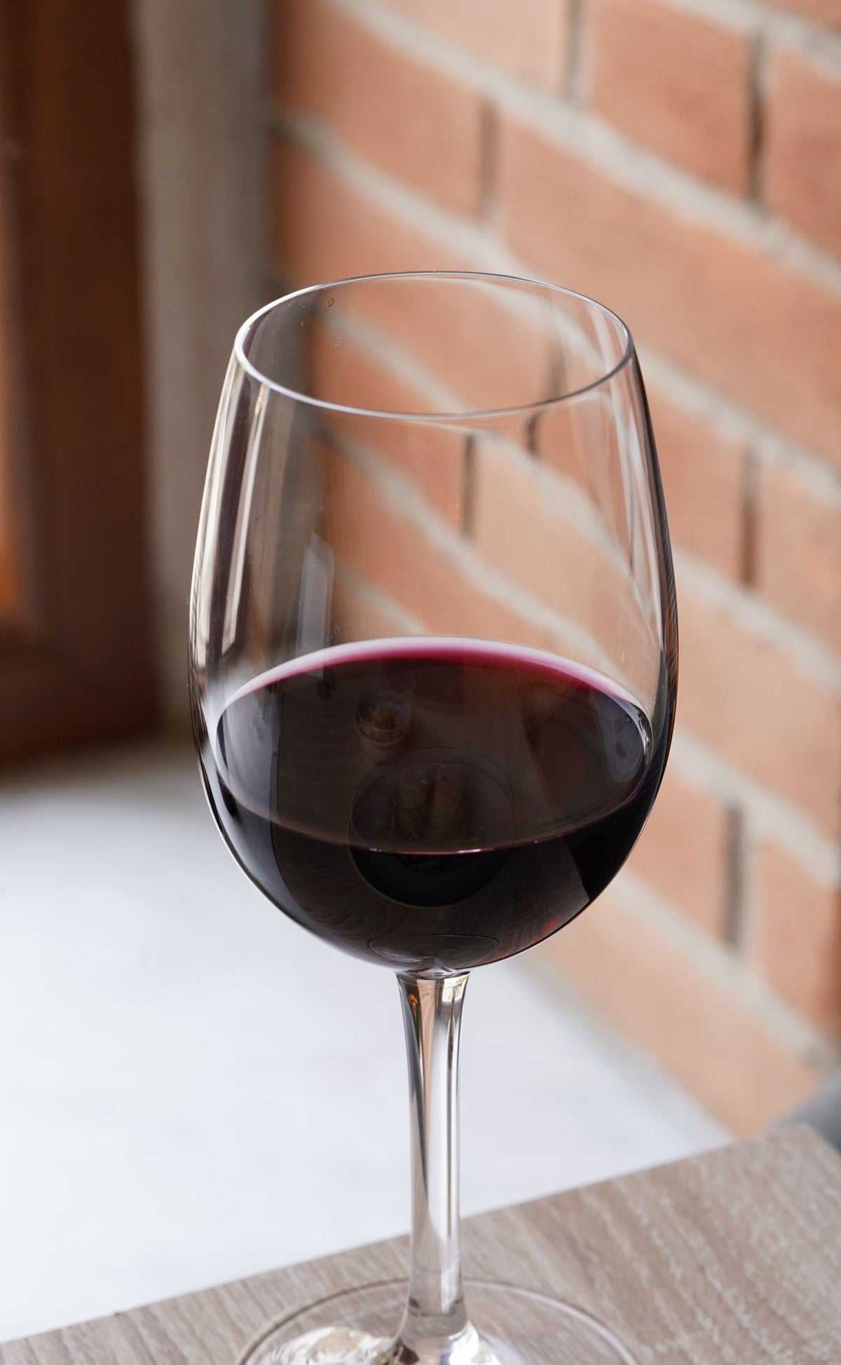 A glass of red wine on a table against a brick wall