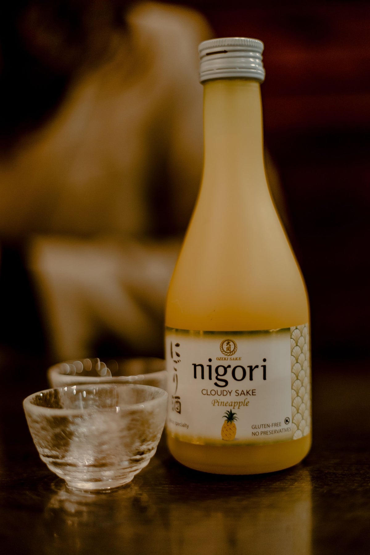 Chilled cloudy sake in a glass carafe beside two small cups on a wooden table