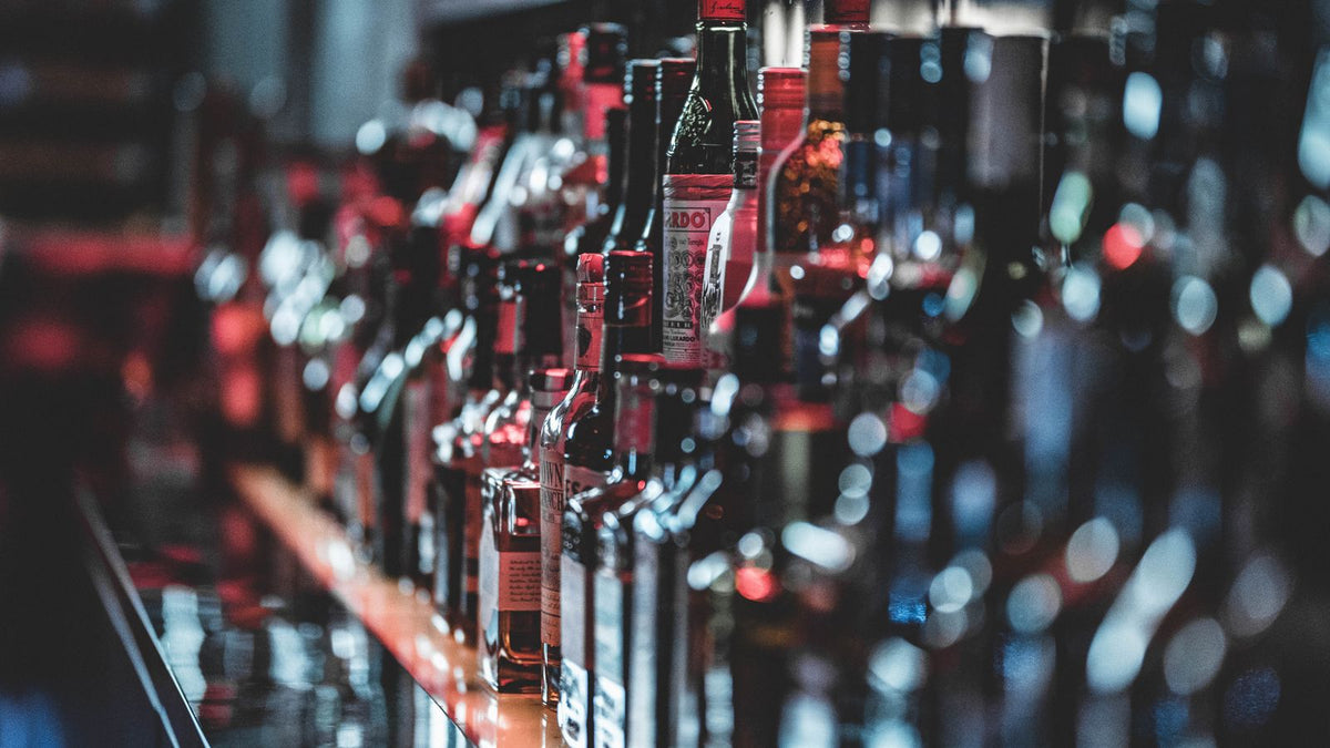 A row of liquor bottles lined up along a bar shelf, softly out of focus