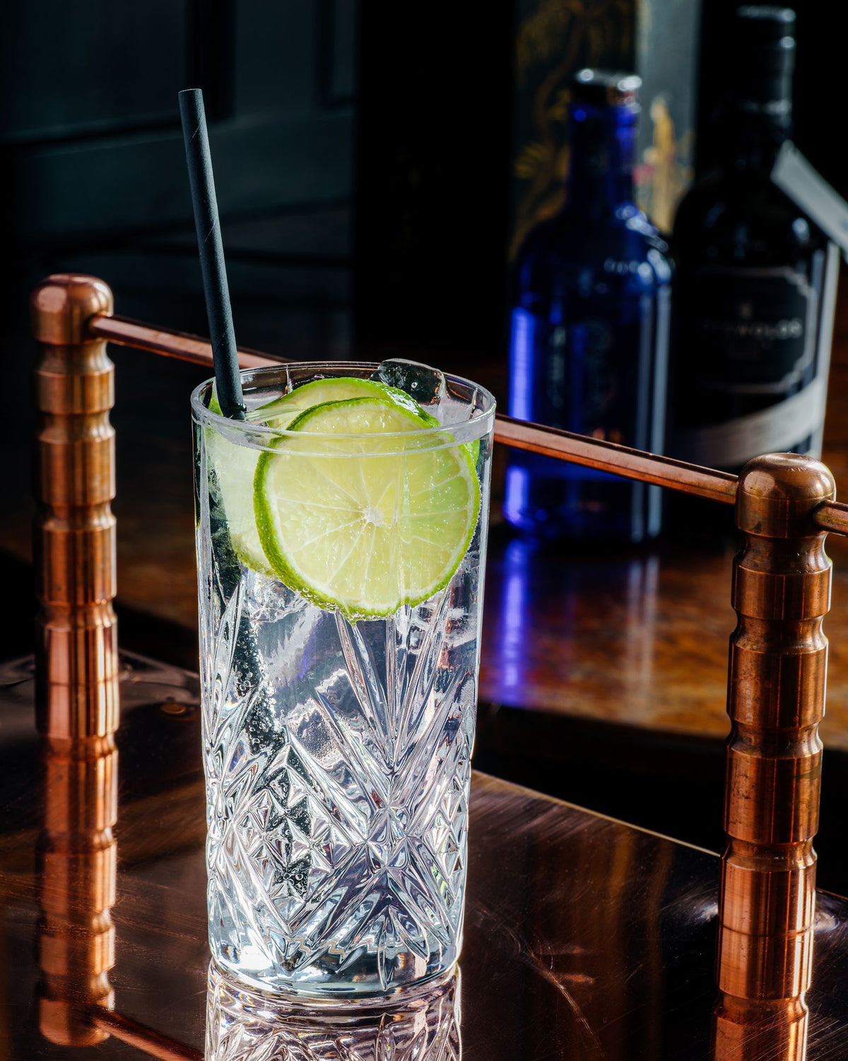 A gin and tonic with lime slices in a crystal glass on a copper bar top