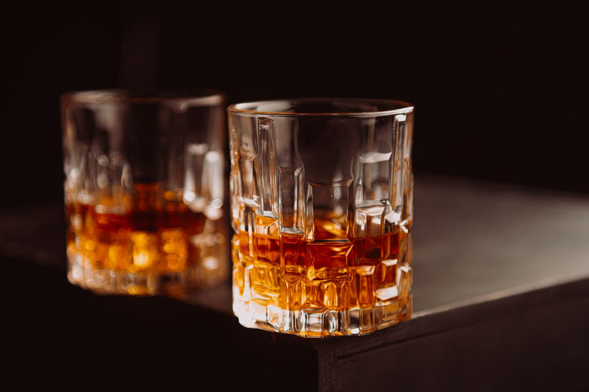 Two cut crystal glasses of amber whisky on a dark wooden surface