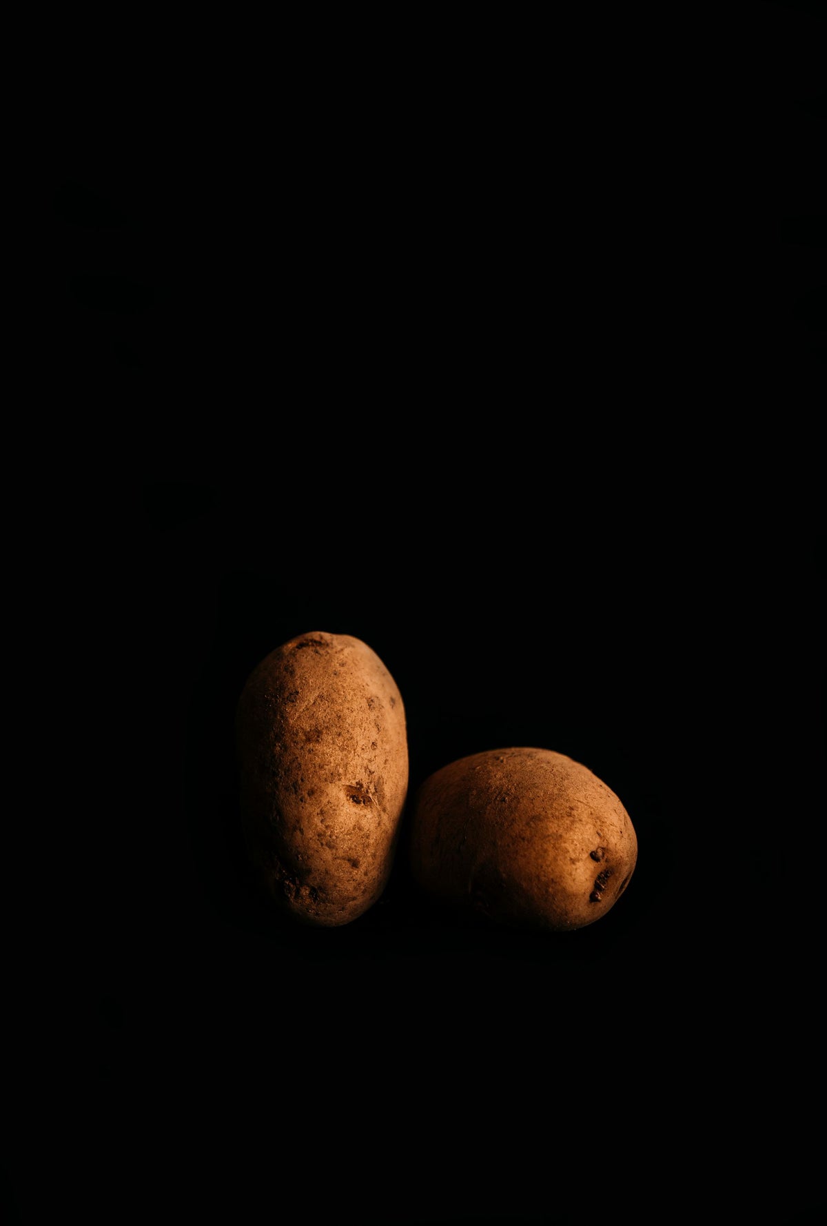 Two raw potatoes lit warmly against a black background