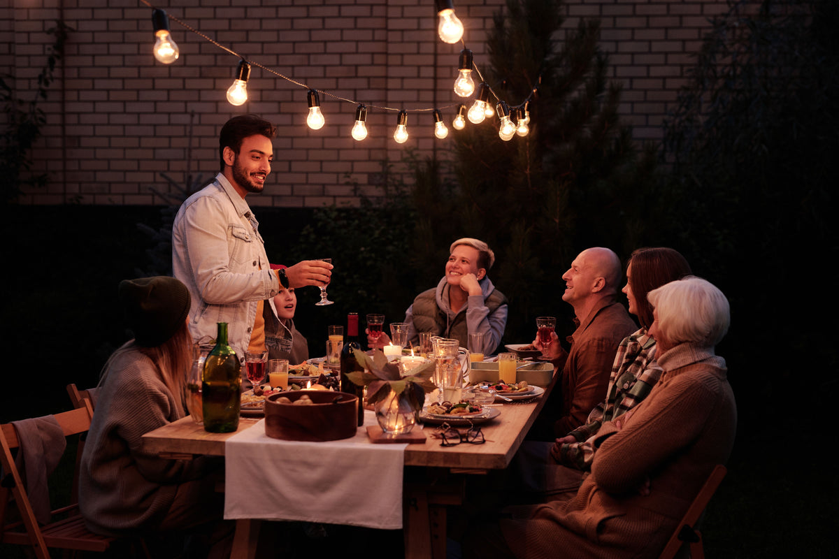Guests eating together at an outdoor table under warm string lights
