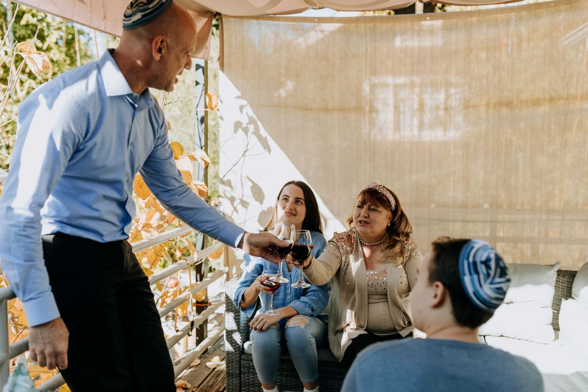 A family raising glasses of red wine together in a sukkah, autumn leaves and matting overhead