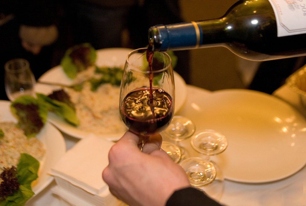 Red wine being poured into a glass at a set dinner table