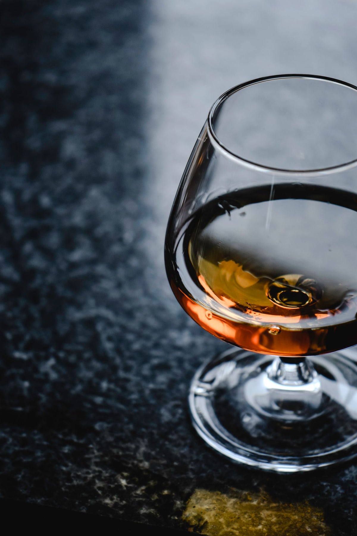 Amber cognac resting in a snifter glass on a dark stone surface