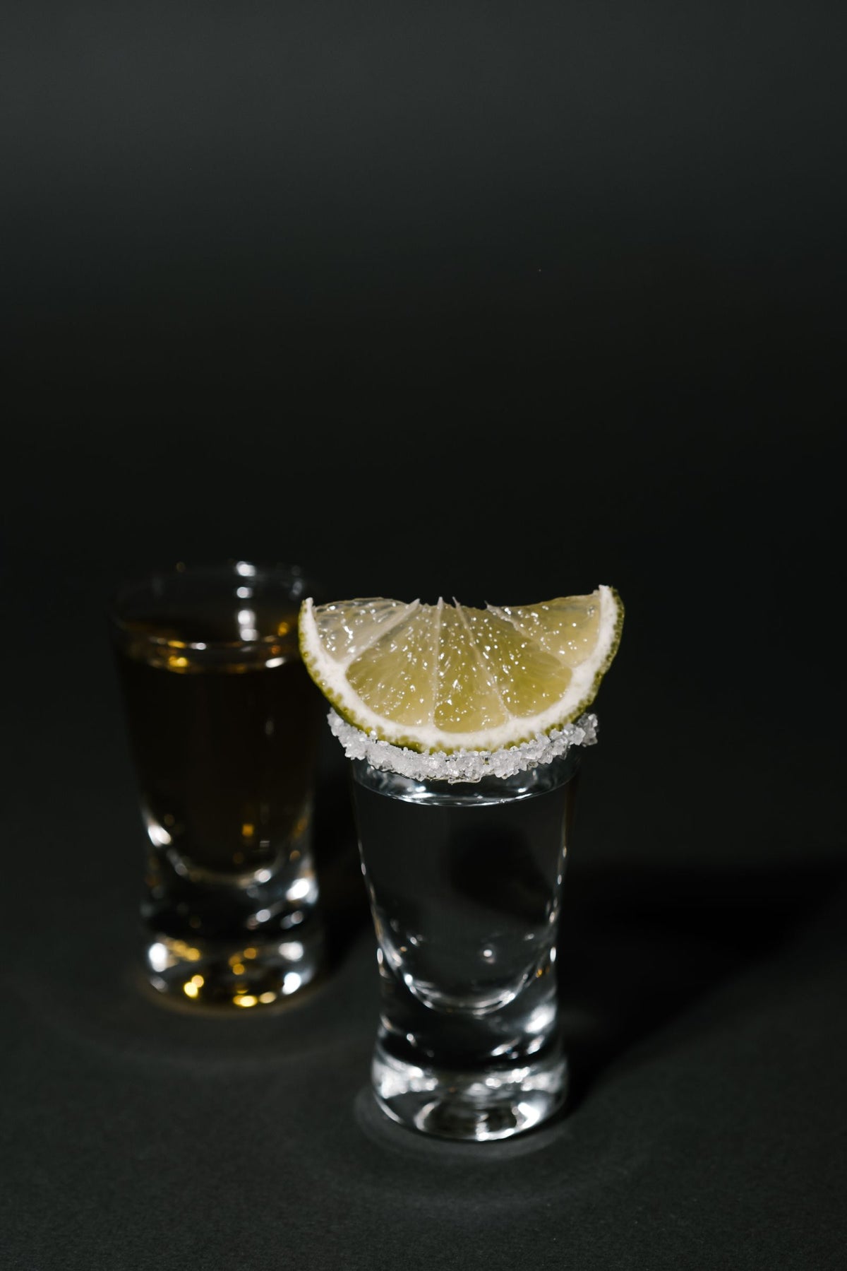 Two tequila shots with lime and salt on a dark bar
