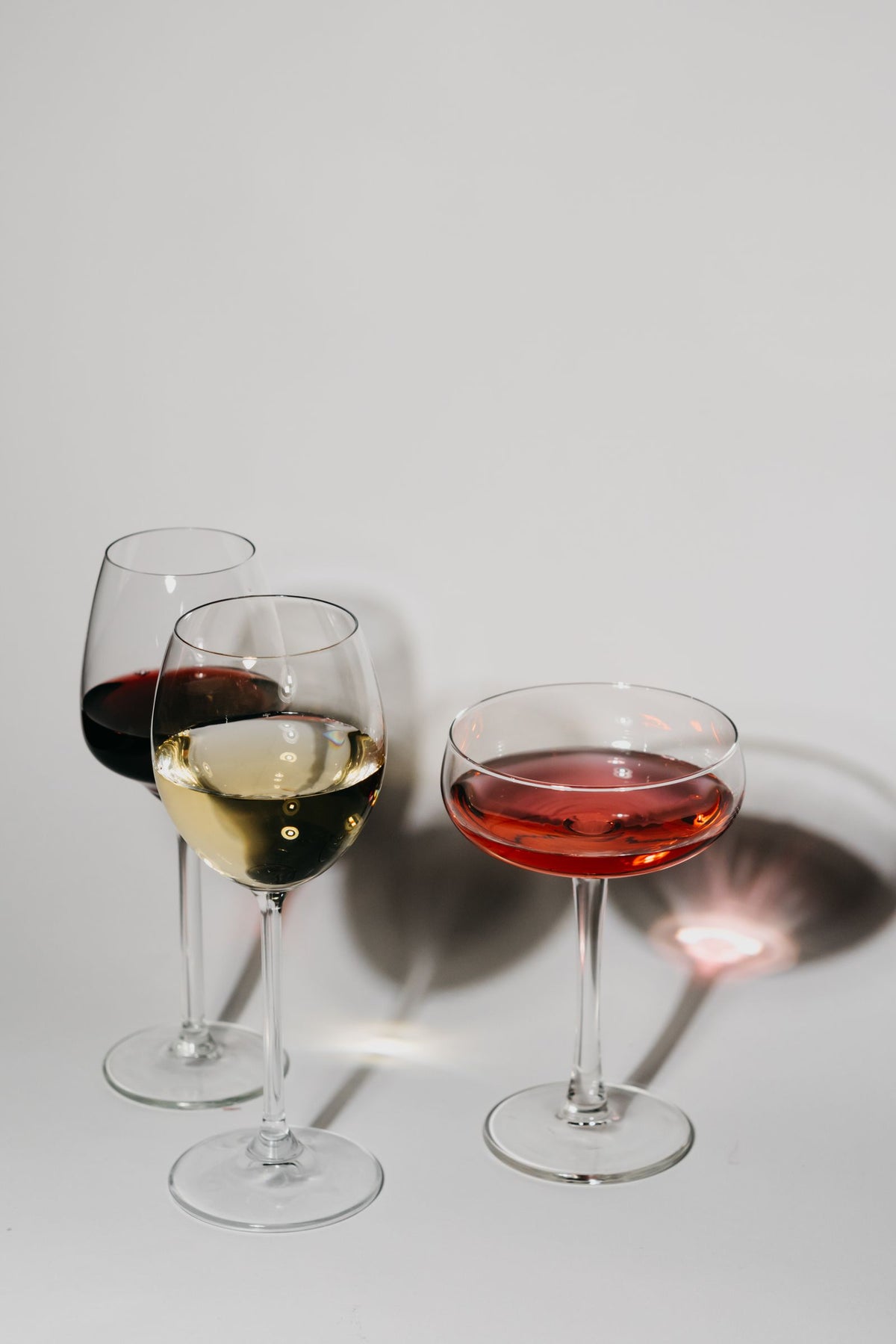 Three wine glasses holding red, white and rose wine on a pale background