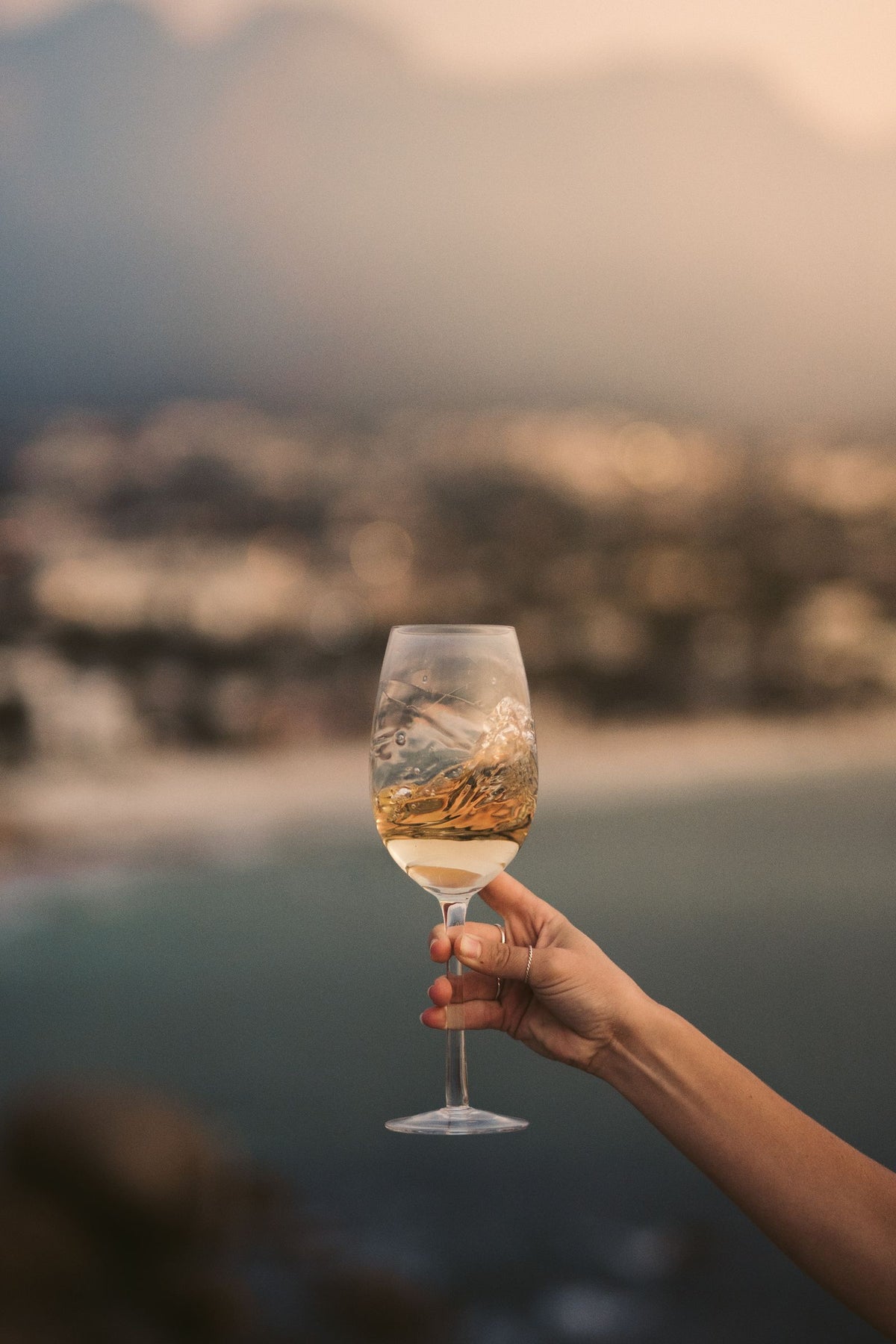 A hand holding a glass of white wine with a scenic coastal backdrop