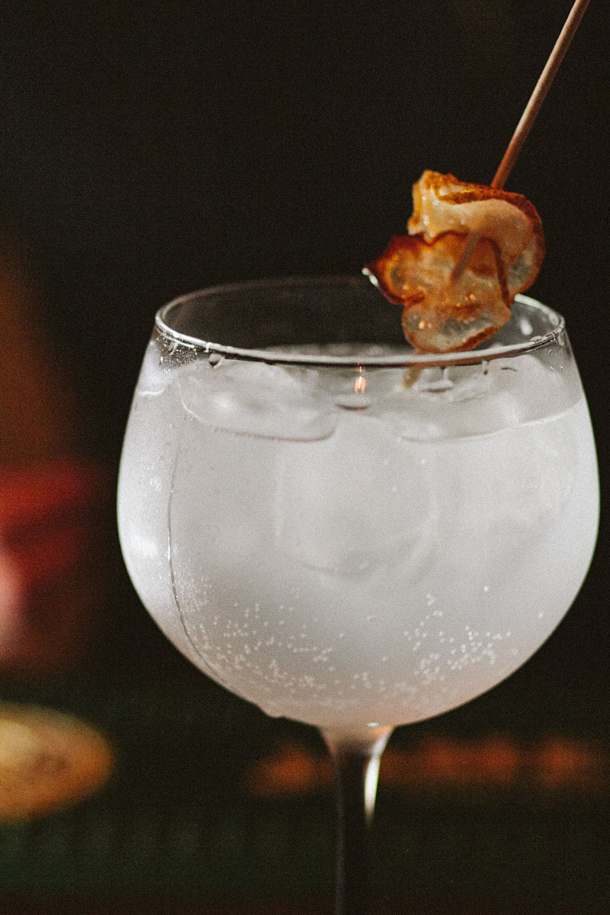 A gin and tonic with ice and a citrus garnish on a bar top