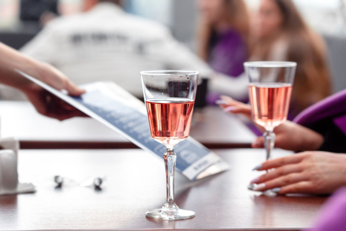 Two glasses of chilled pink rose wine on a wooden table, friends talking in the background