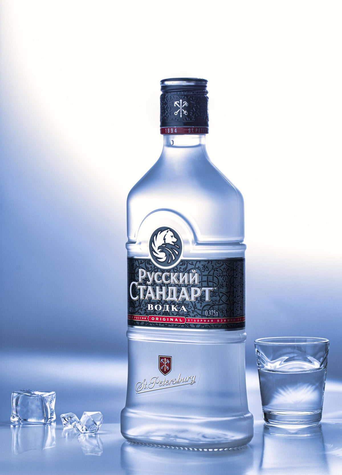A bottle of Russian Standard vodka beside a chilled shot glass and ice