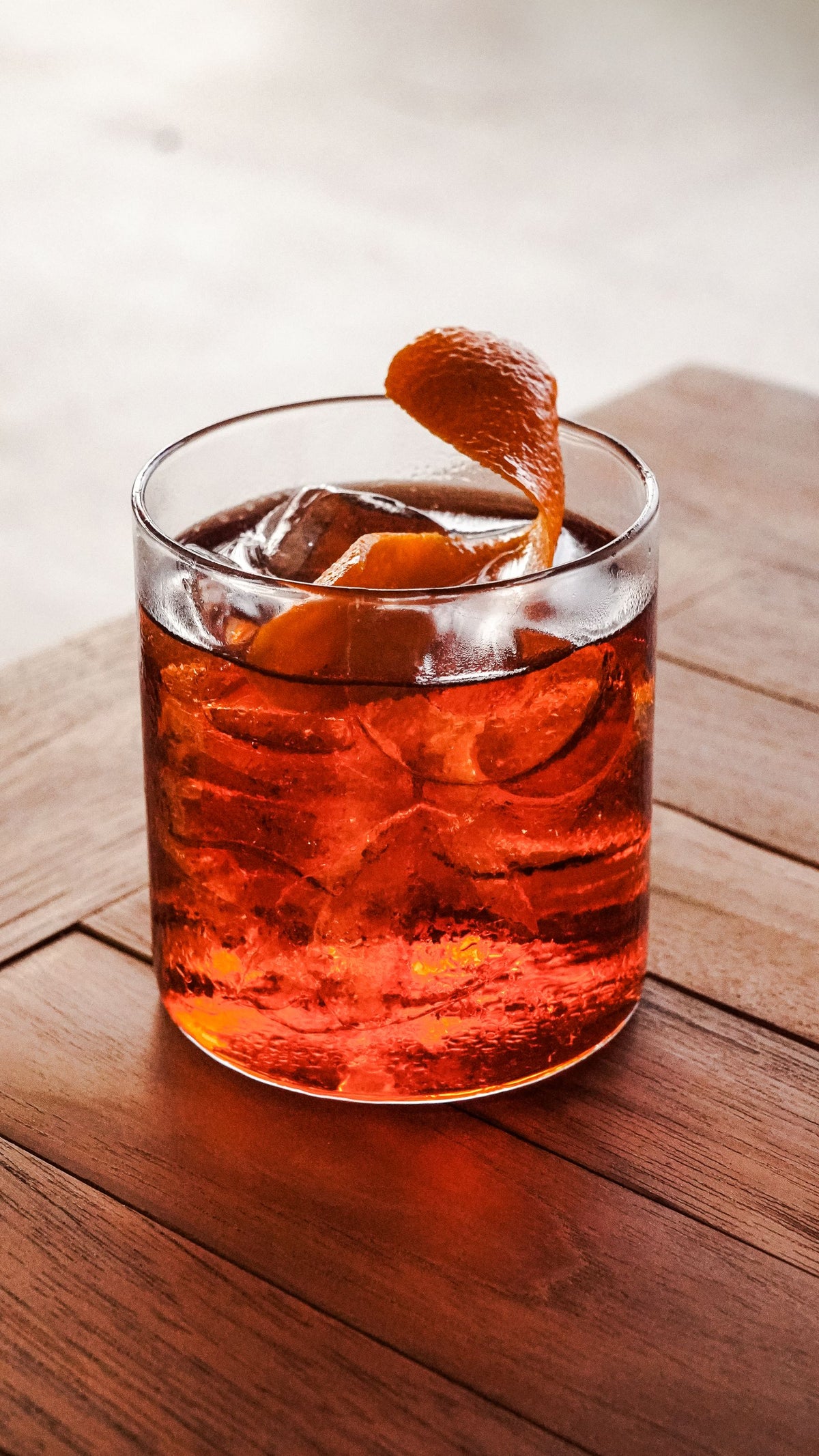 A Negroni cocktail over ice with an orange peel on a wooden table