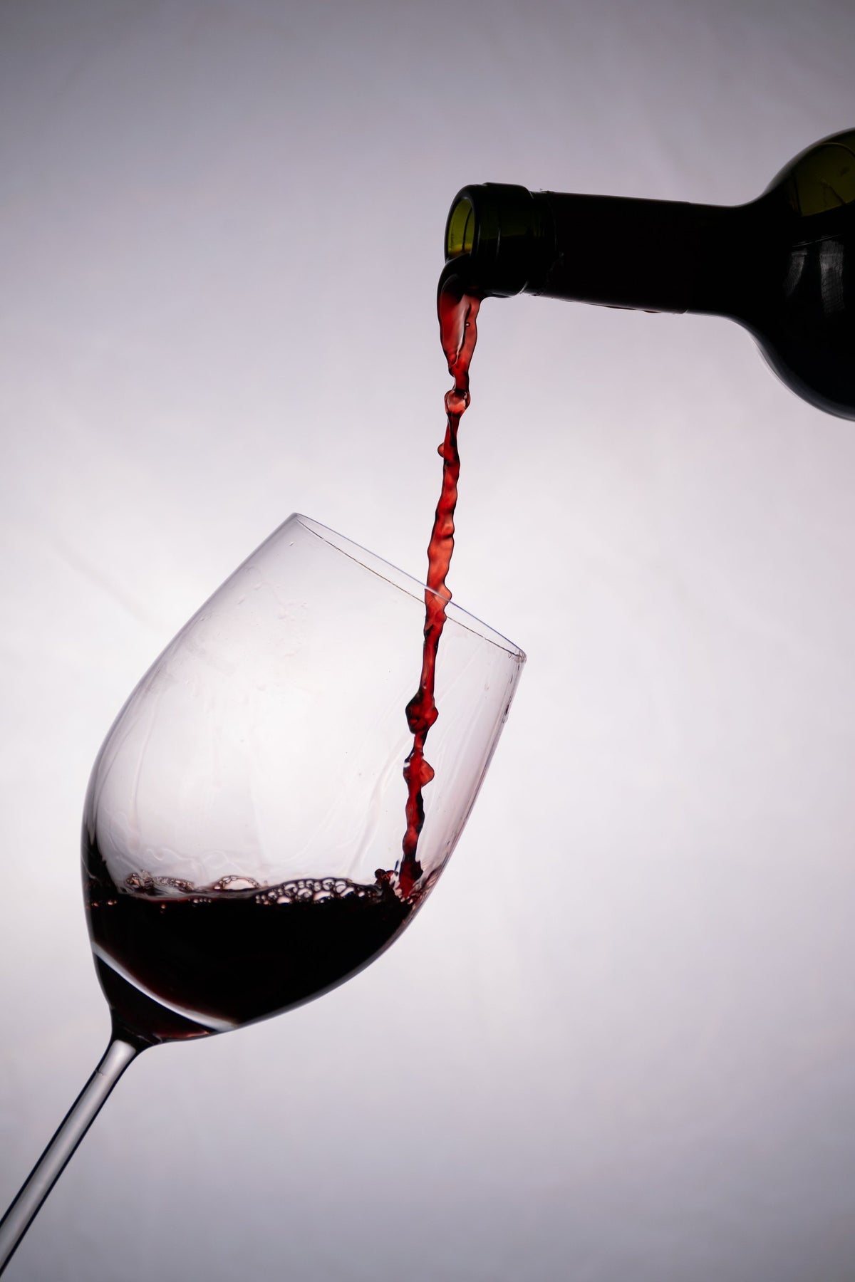 Red wine pouring from a dark bottle into a tilted wine glass in a studio setting