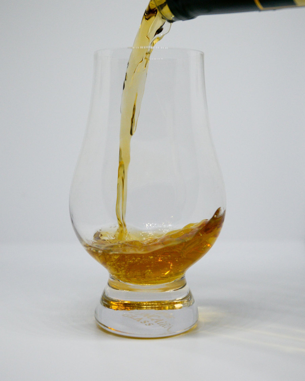 Whisky being poured into a Glencairn nosing glass against a clean white background