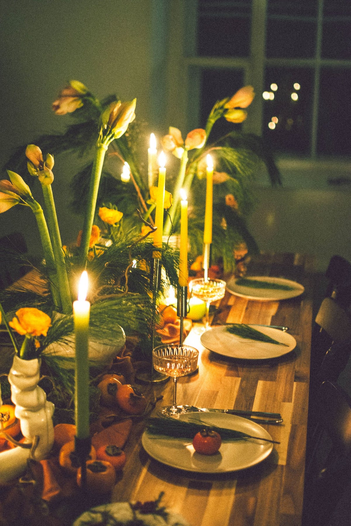 A candlelit table set for a yom tov meal with plates, glasses and flowers