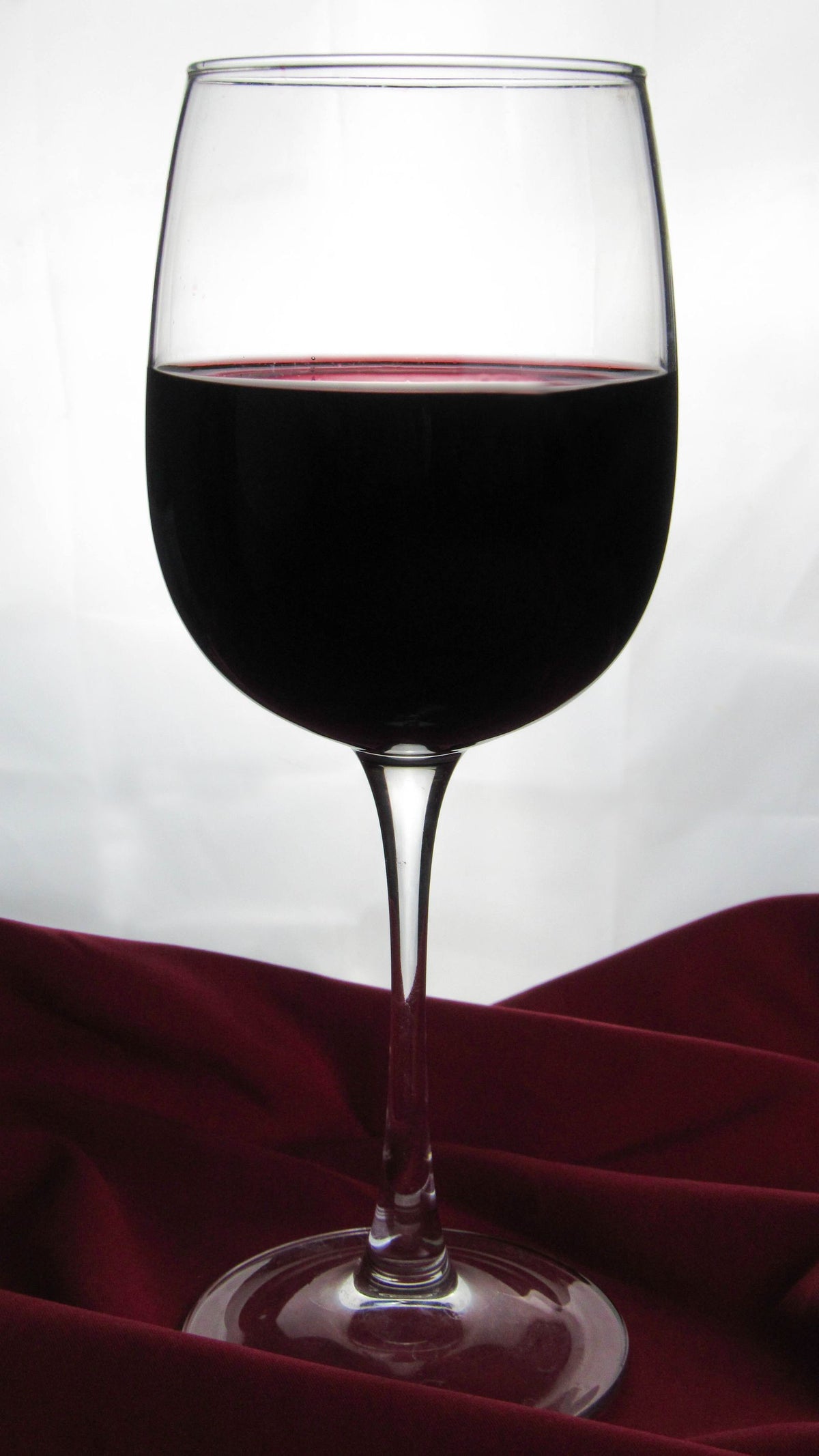 Close-up of a single glass of red wine against a moody velvet backdrop