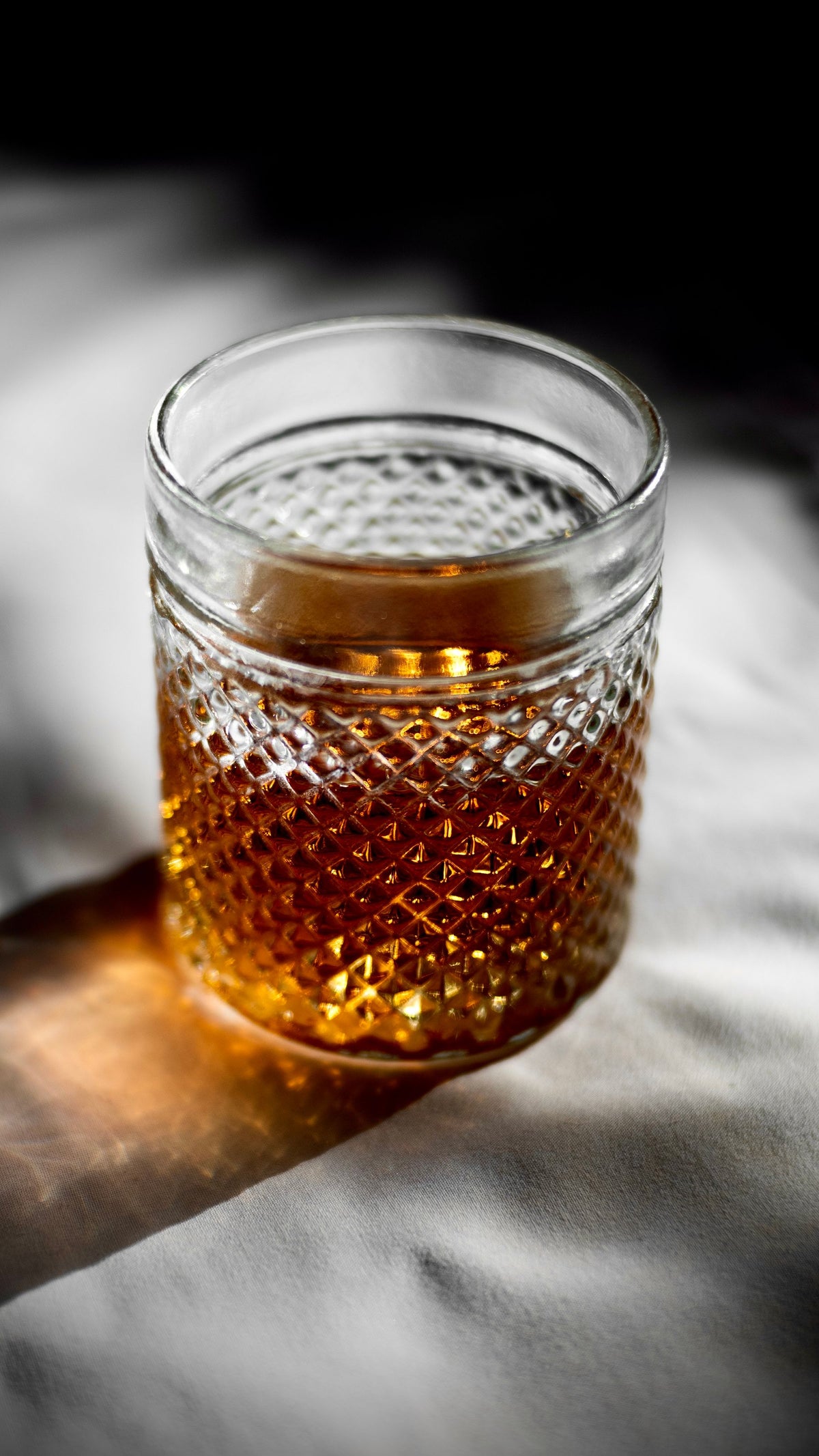 A crystal glass of amber liqueur catching warm light on a dark surface