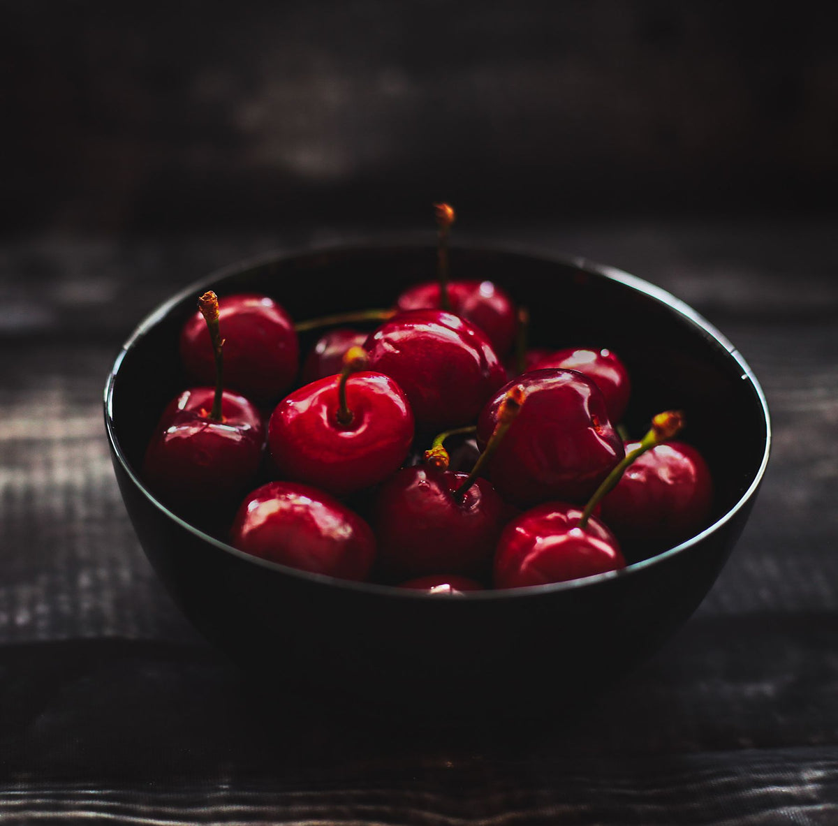 Dark red cherries in a black ceramic bowl on a rustic table