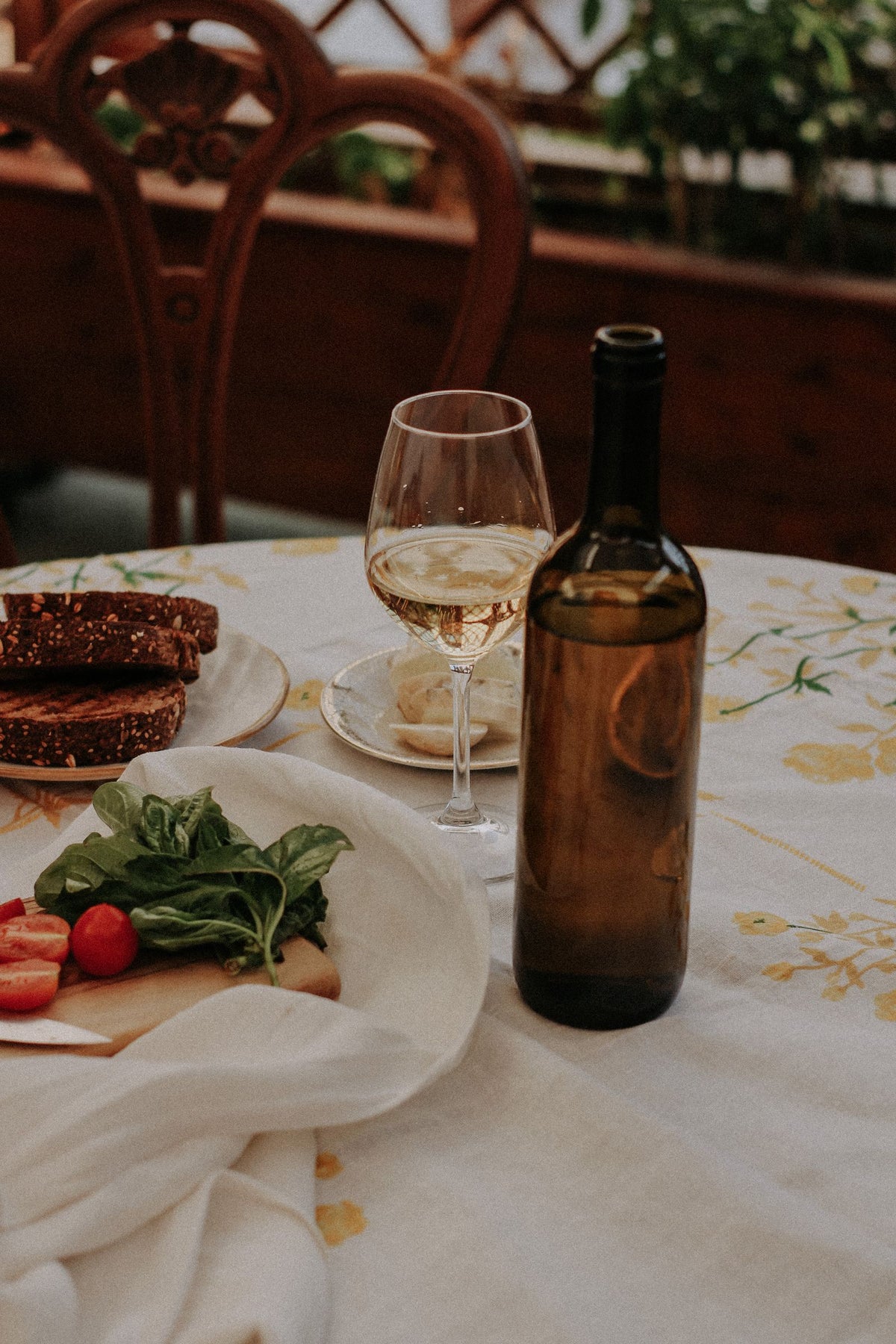 Wine bottle and a poured glass on a set table with bread, tomatoes and fresh basil