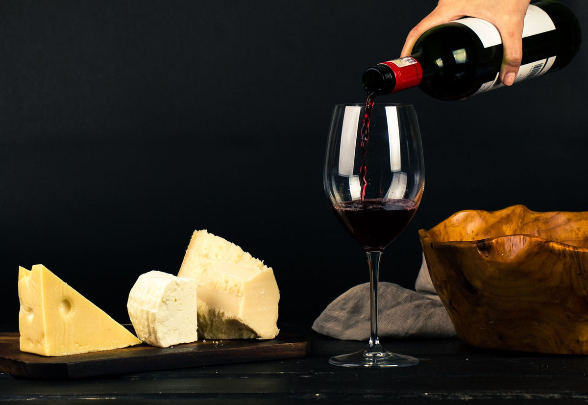 Red wine poured into a glass beside cheese