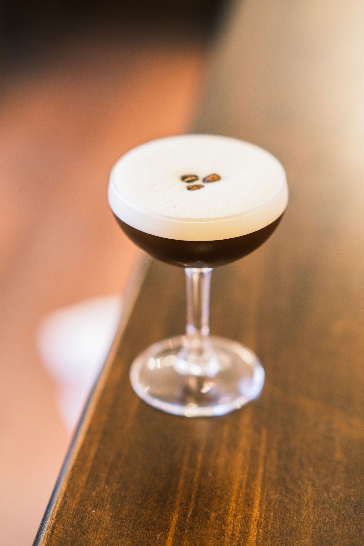 An espresso martini with three coffee beans on the foam, on a wooden bar