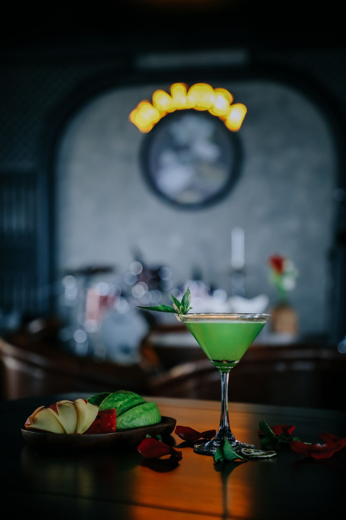 A green apple martini in a stemmed glass on a bar counter with fresh fruit
