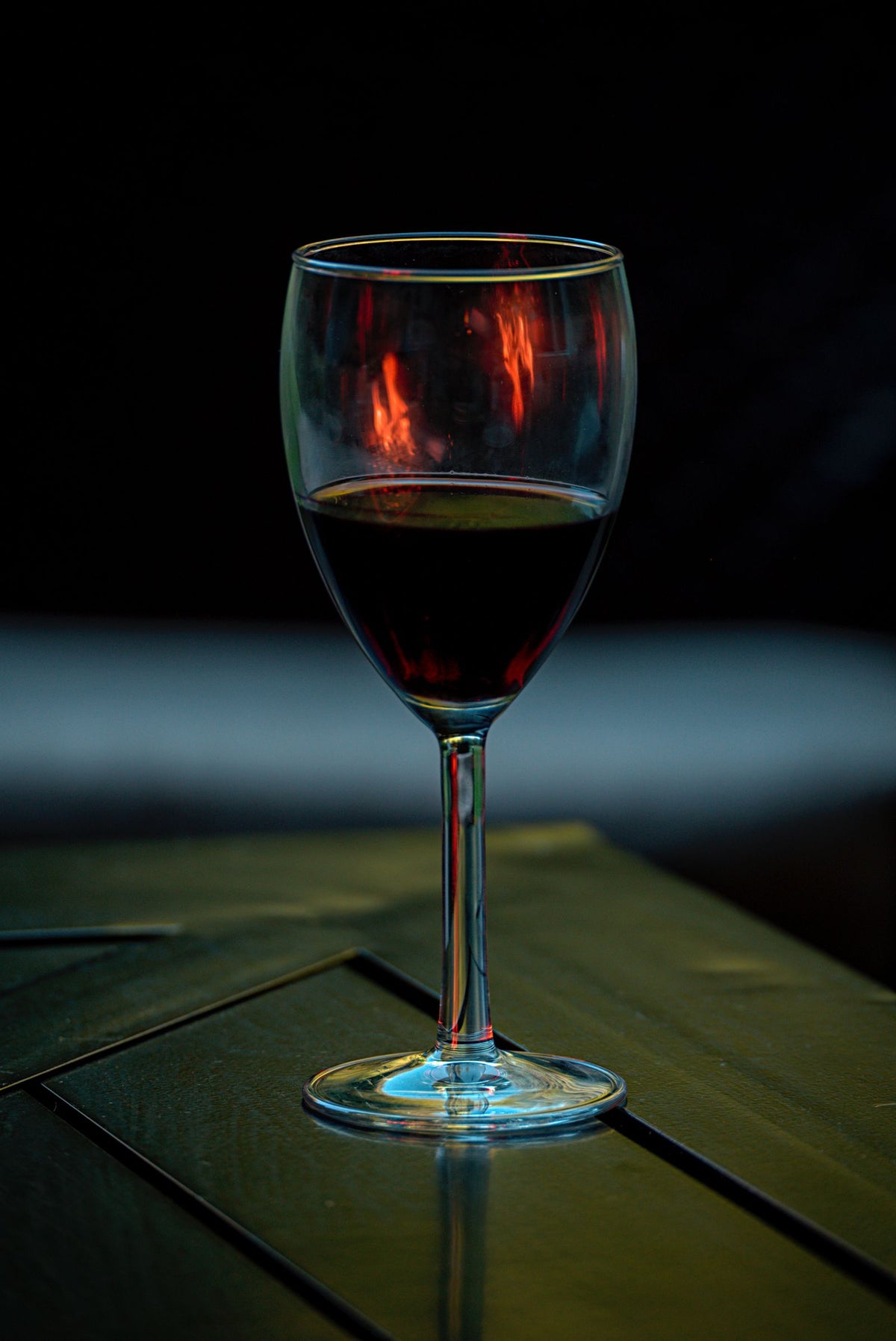 A single glass of red wine on a wooden table against a dark background