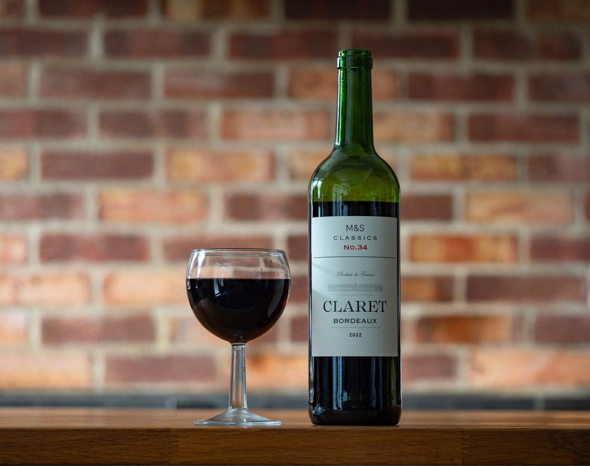 A bottle of red Bordeaux and a filled glass on a rustic wooden table