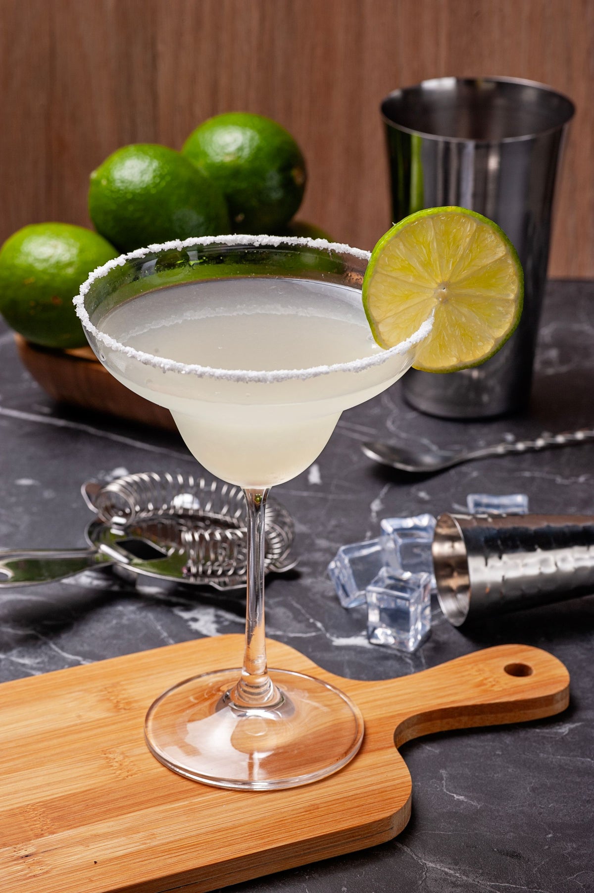 A classic margarita with a salted rim and a lime wedge on a wooden board