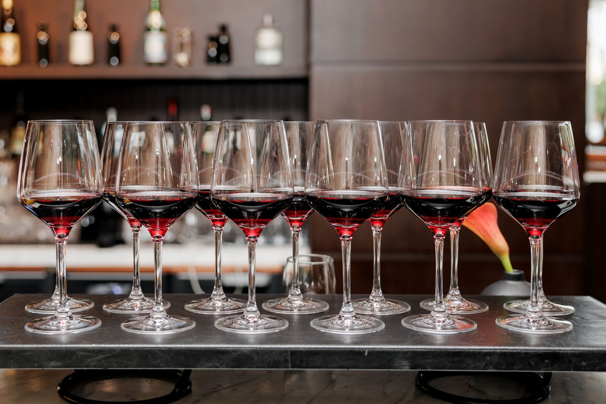 A row of red wine glasses poured and lined up on a bar counter