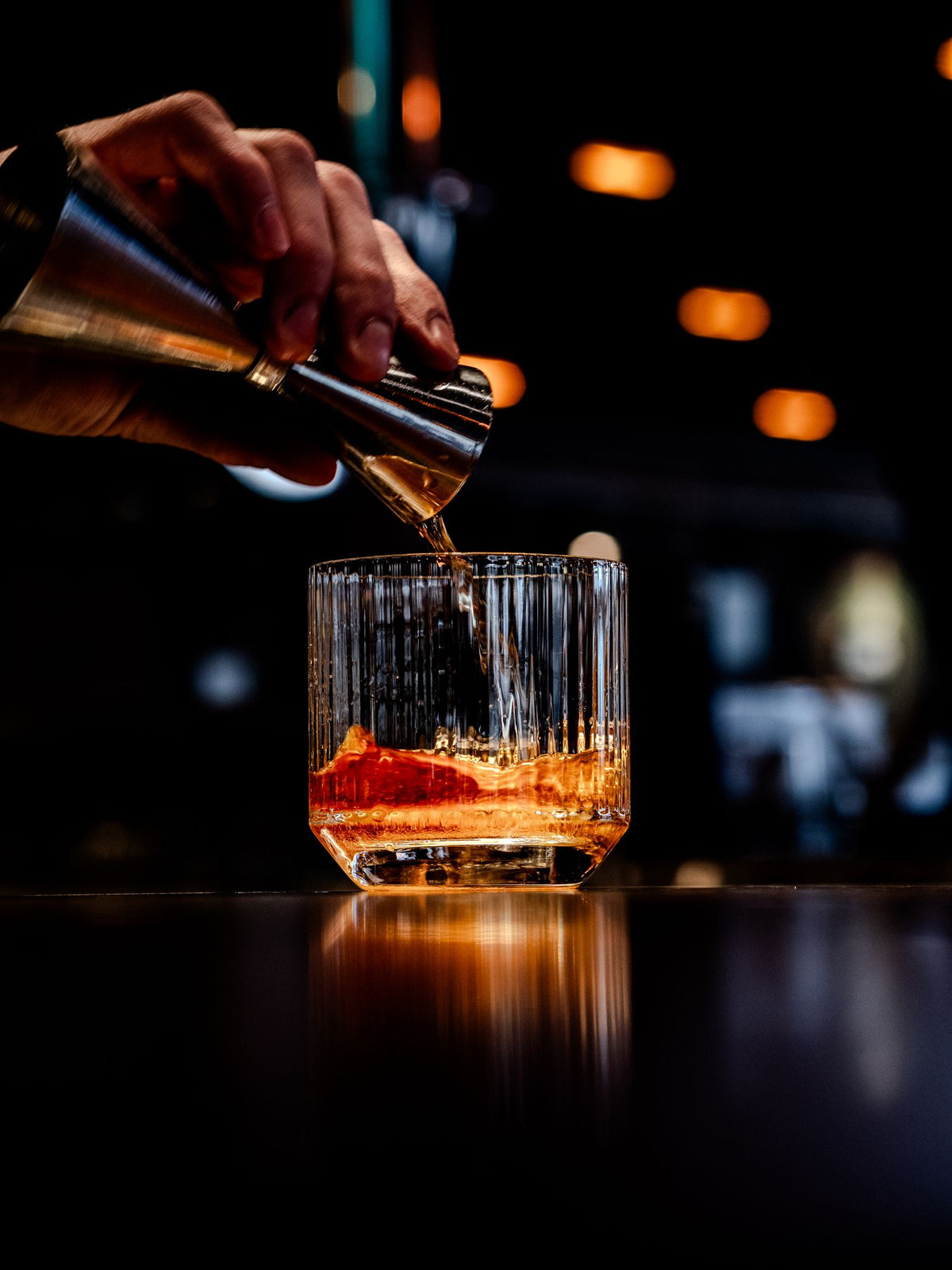 Whiskey being poured over ice in a glass at a dimly lit bar