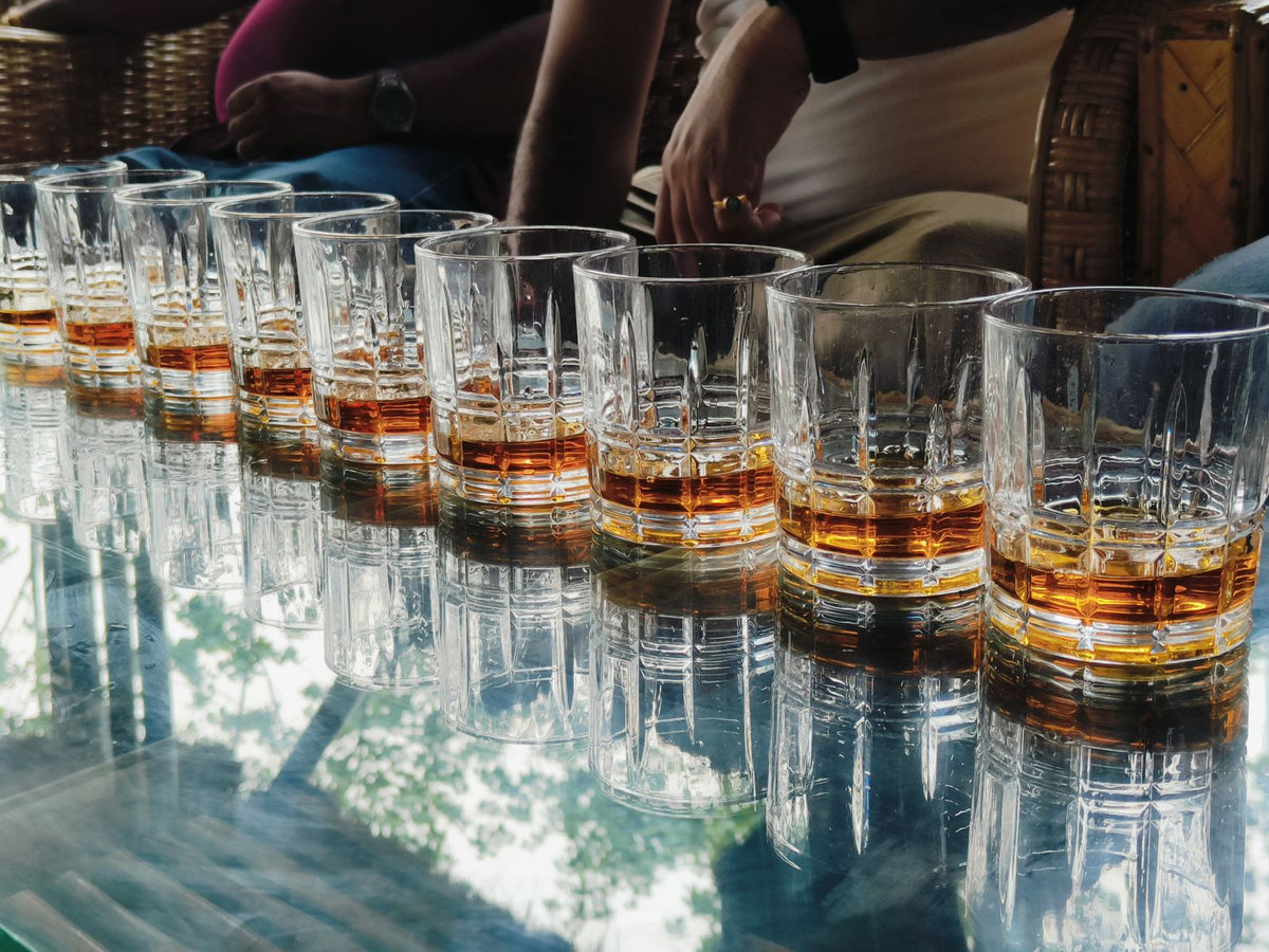A row of whiskey glasses lined up on a bar table