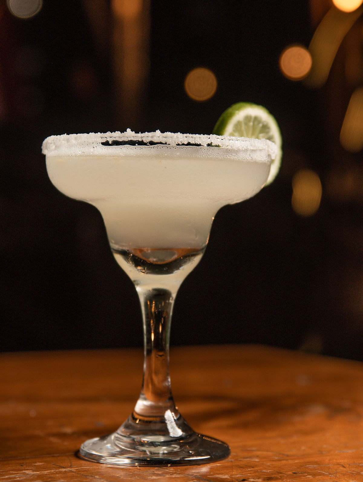 A margarita with a salted rim and a lime wheel on a wooden bar