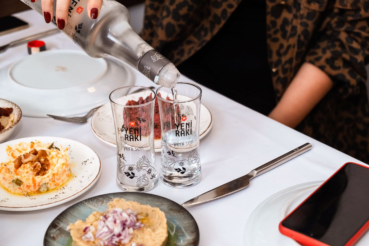 A clear anise spirit being poured at a table set with mezze dishes