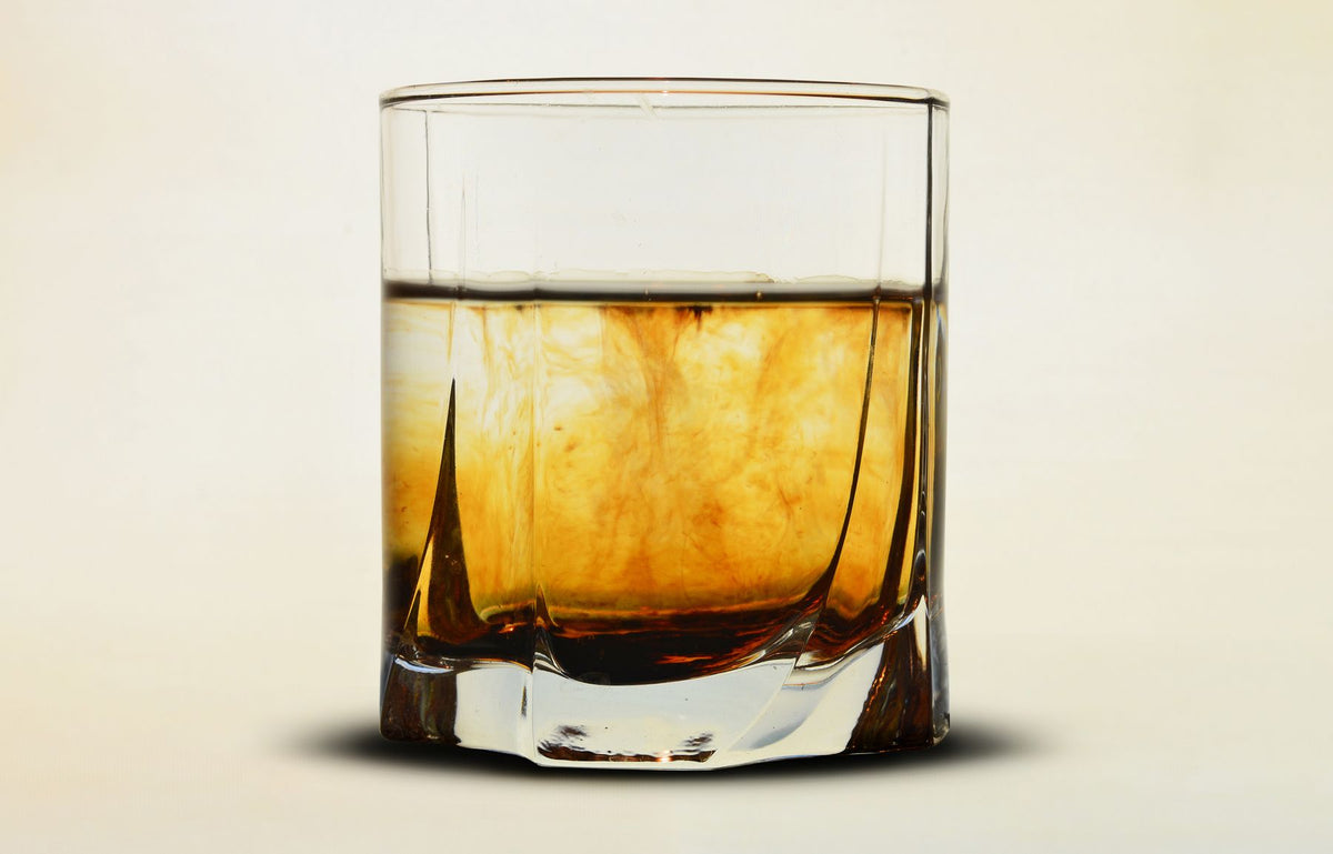 A glass of amber whisky on a plain neutral background