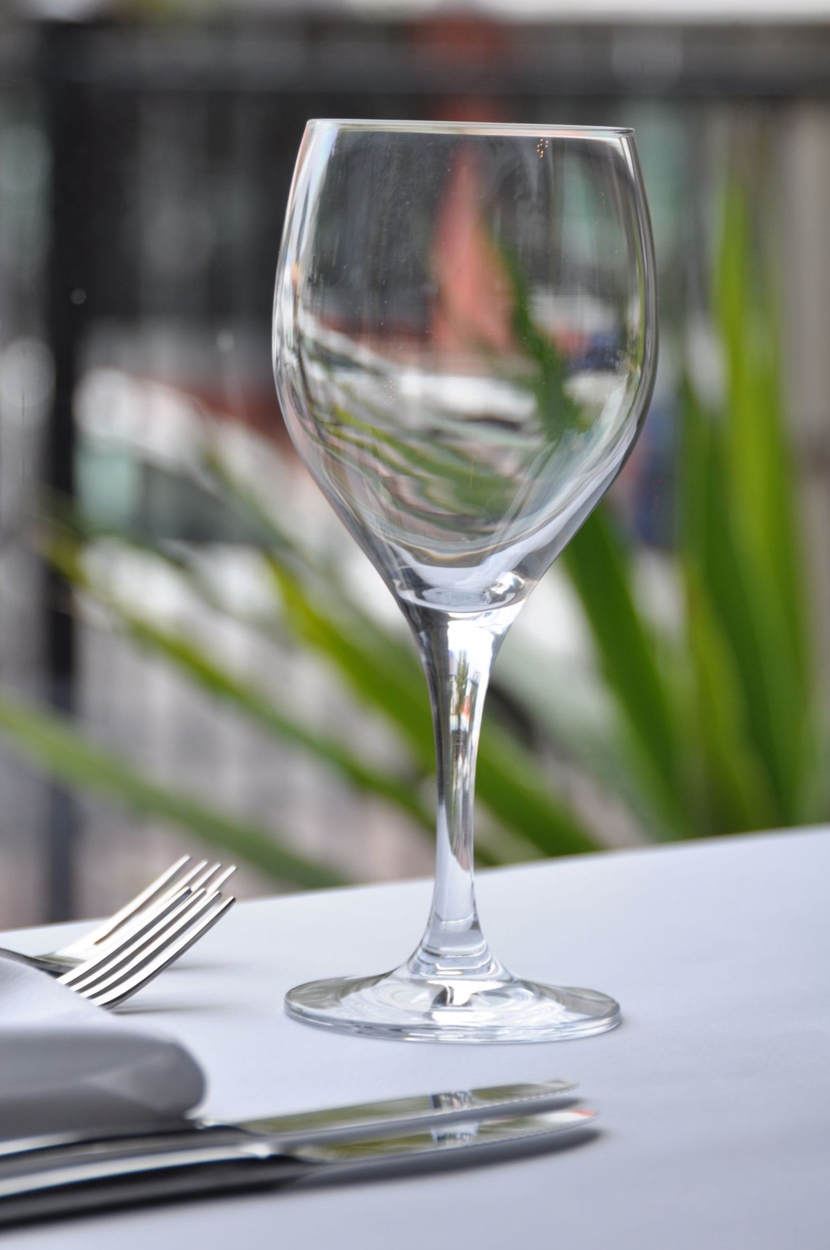 A wine glass on a set dining table with cutlery and a blurred background