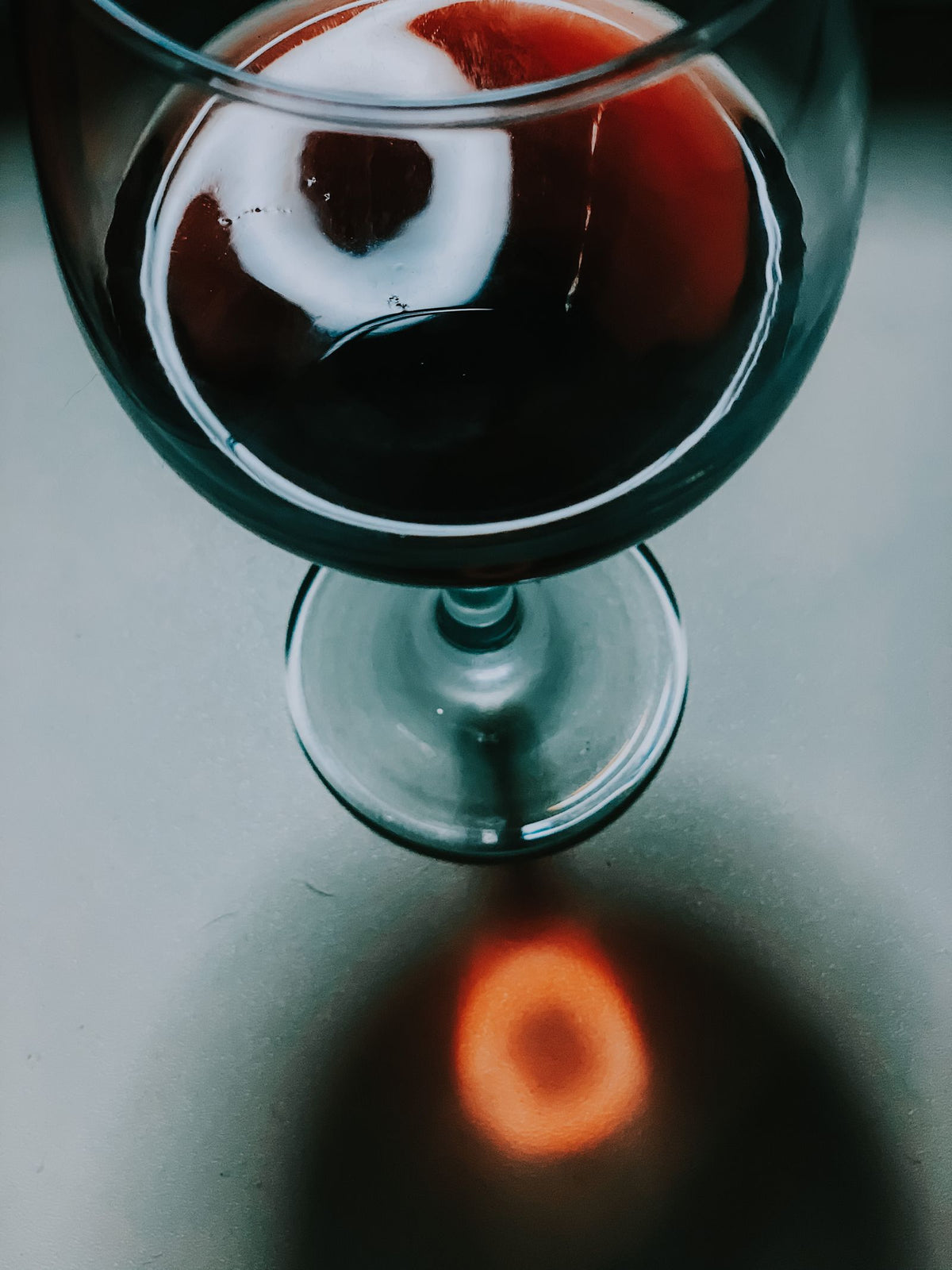 An overhead view of a glass of red wine on a pale table