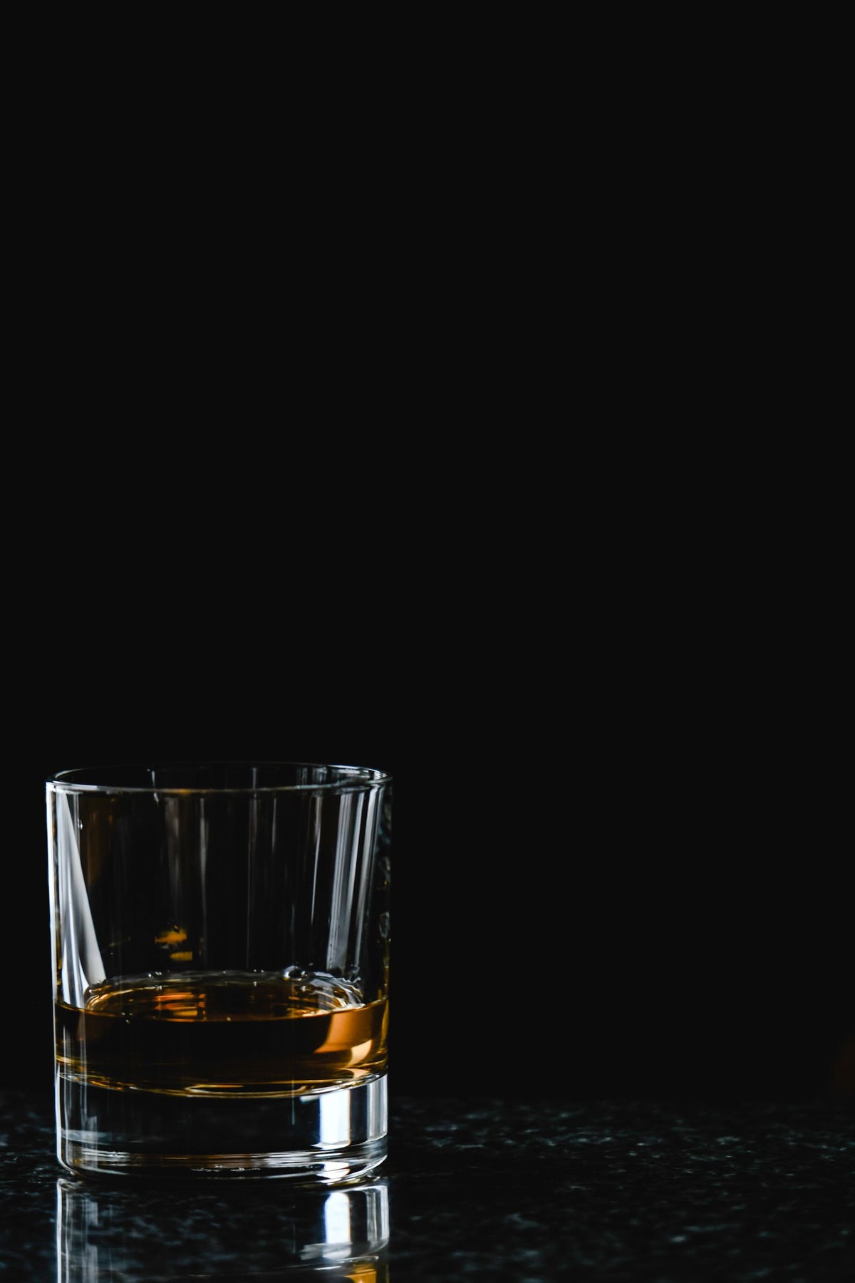 A glass of whiskey resting on a dark polished surface