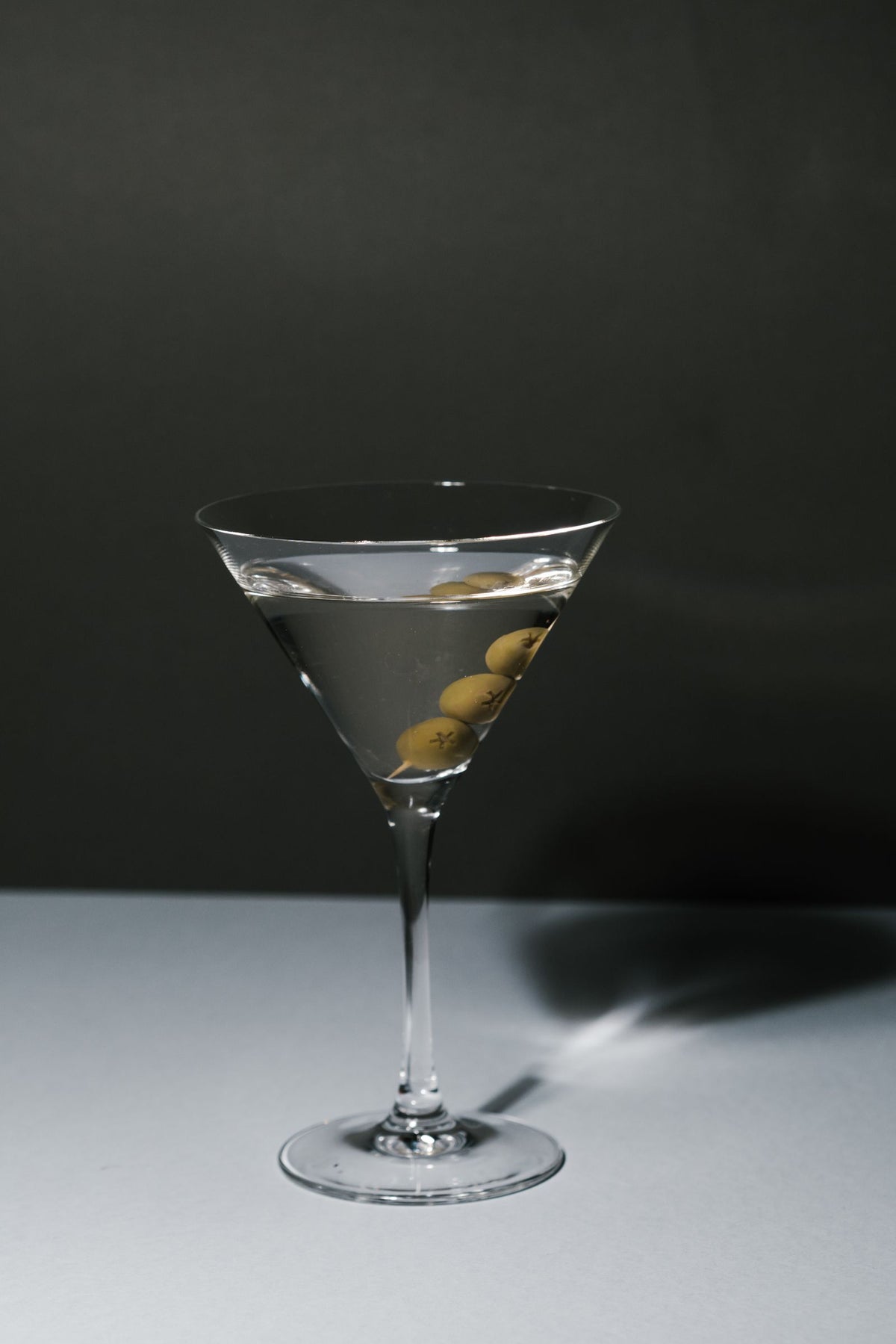 A martini glass with olives against a plain backdrop